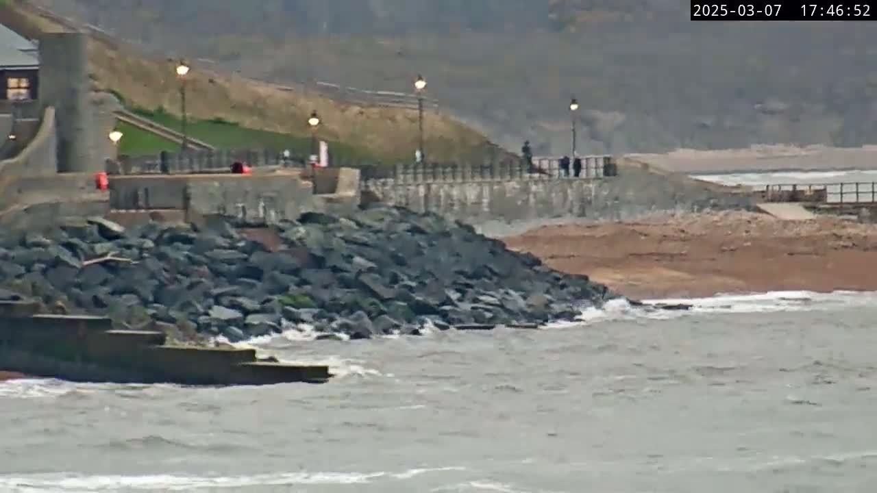 A rocky seawall protects a paved walkway overlooking a choppy gray sea on an overcast day.