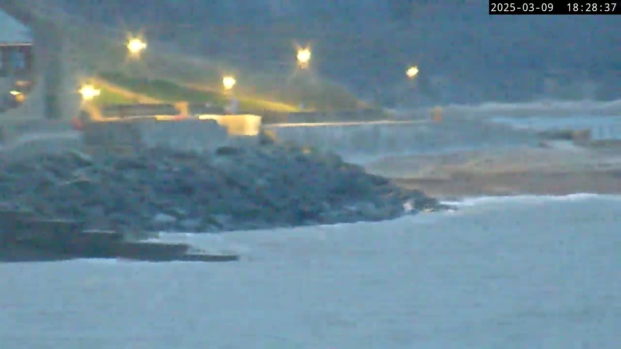 A dark, rocky shoreline is partially submerged in choppy, gray water under a twilight sky.