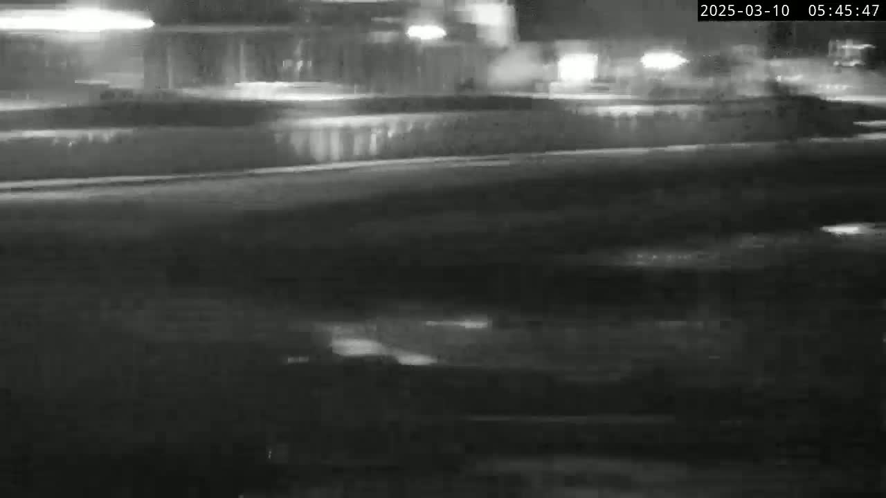 A nighttime, blurry view of a wet road with headlights from moving vehicles in the distance.