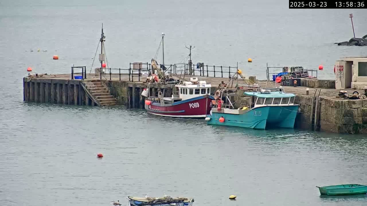 Two fishing boats are moored at a stone pier on a calm, overcast day.