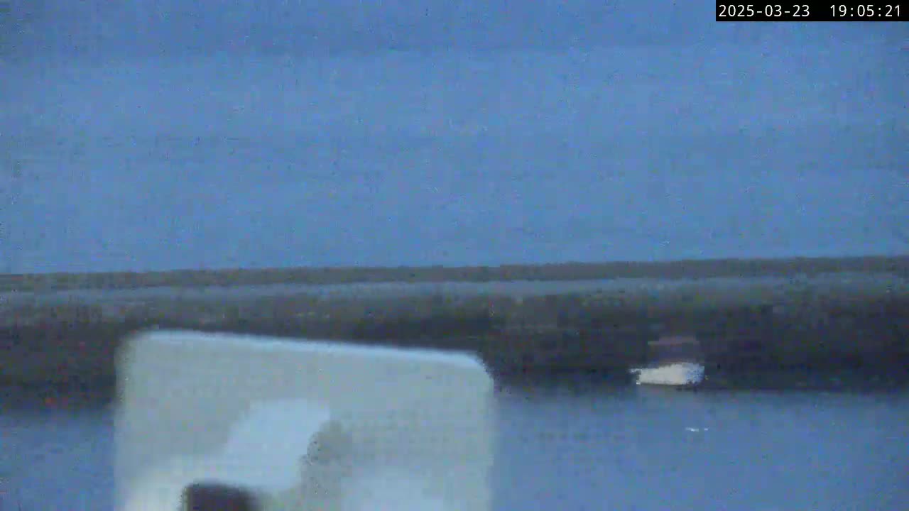 A dark-blue twilight sky hangs over calm water, where a small boat is visible near a dark shoreline.