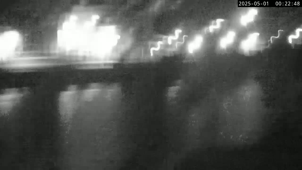 A nighttime, blurry image shows bright lights of vehicles in motion above a dark, reflective surface.