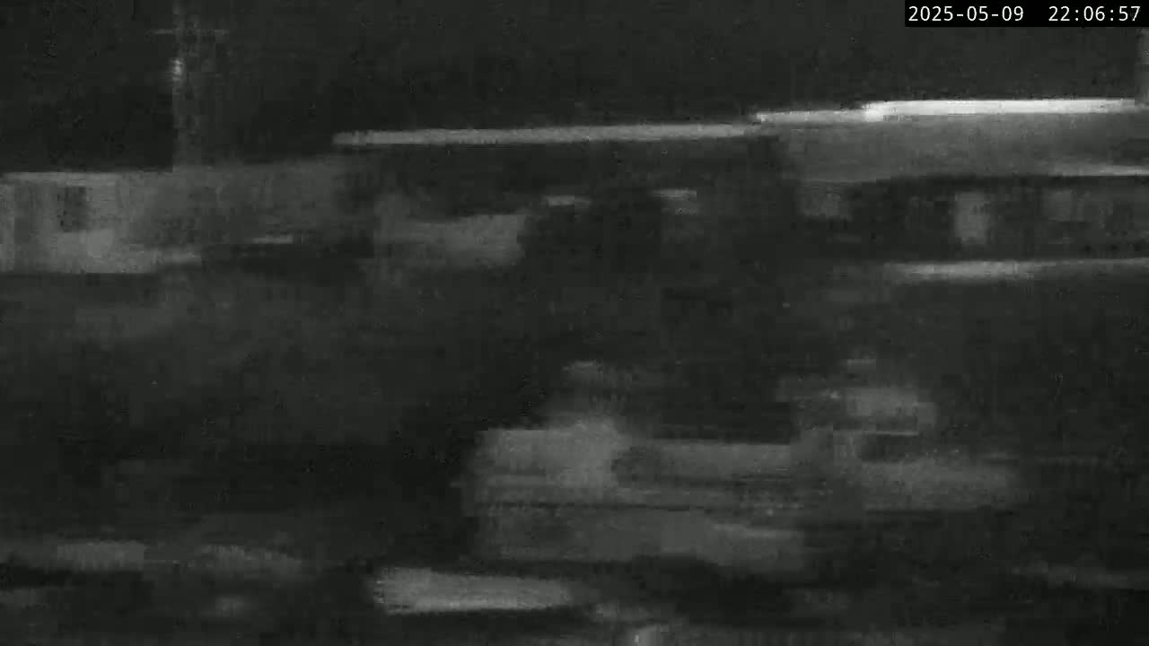 A blurry, nighttime image shows indistinct shapes of buildings and possibly vehicles under dark conditions.