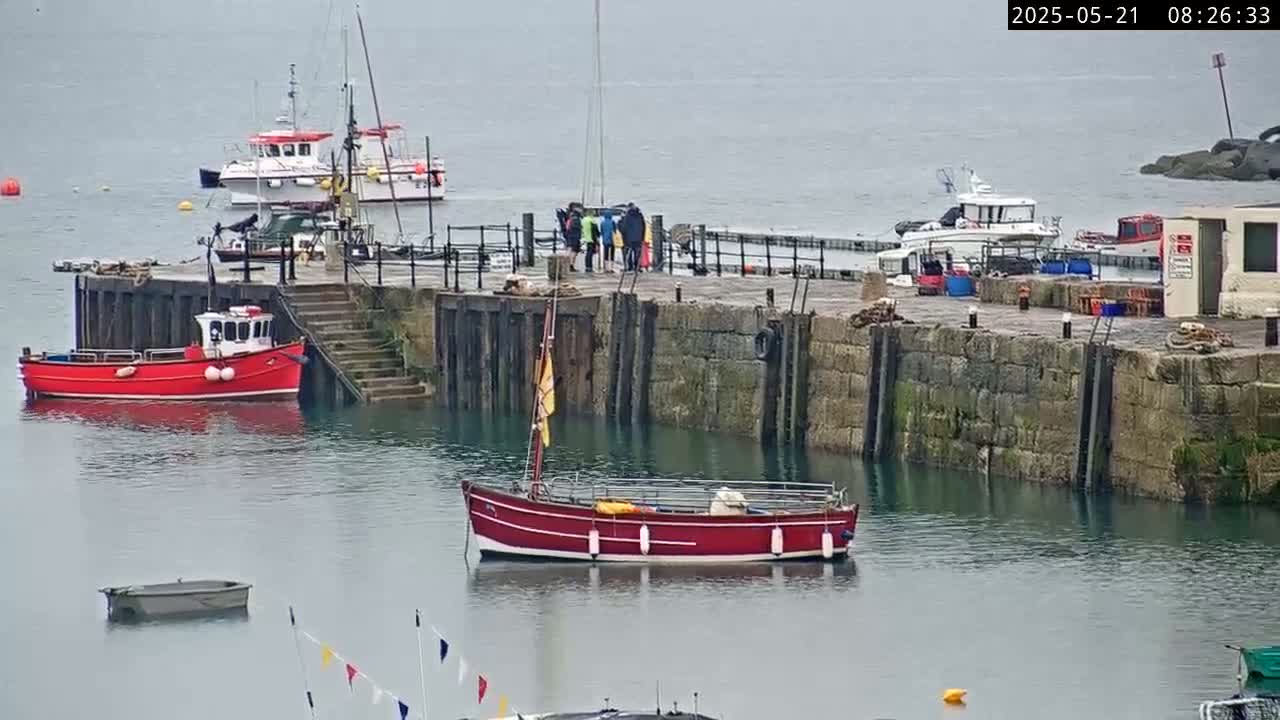 Several boats are moored at a stone harbor wall on an overcast day.