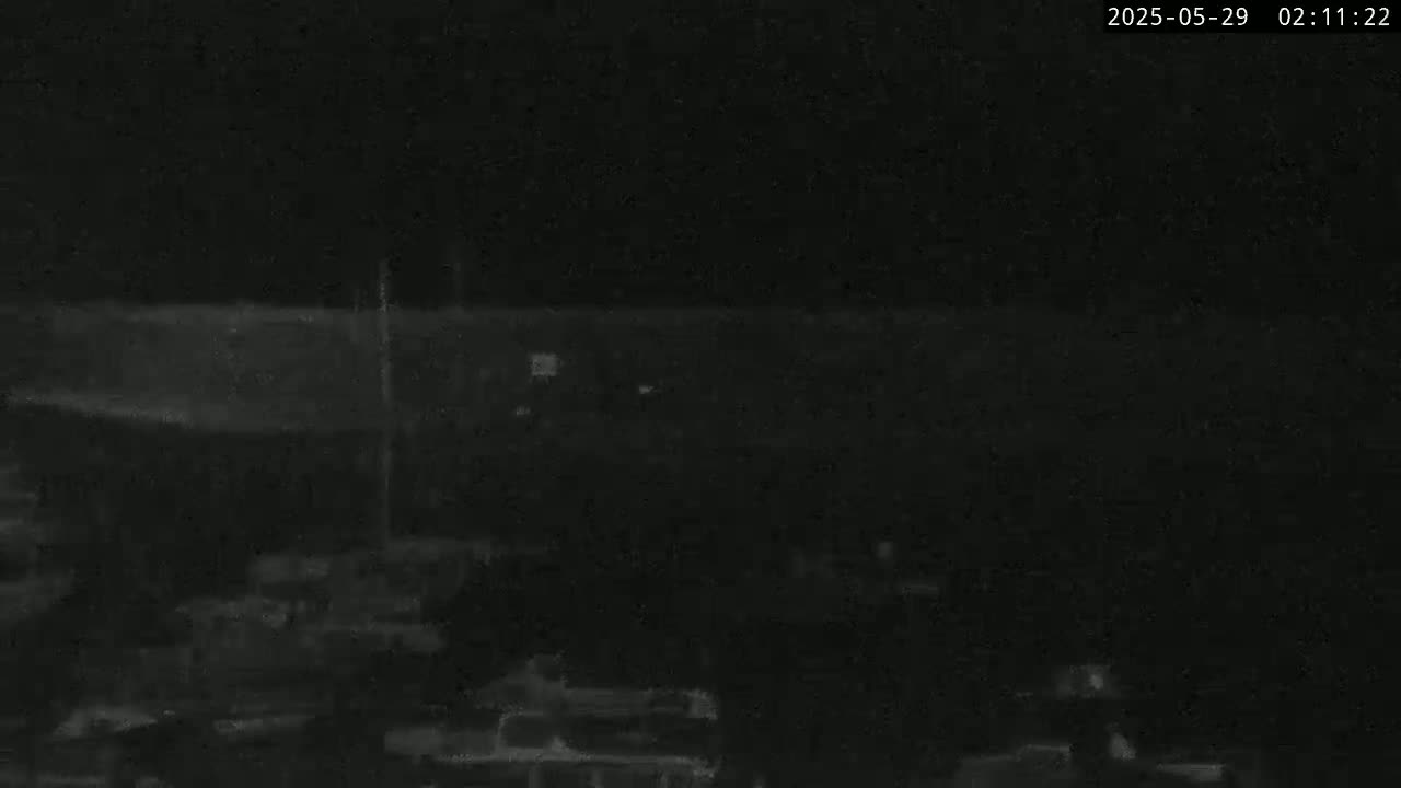 A nighttime, low-light image shows a dark, indistinct area possibly containing structures or vehicles.