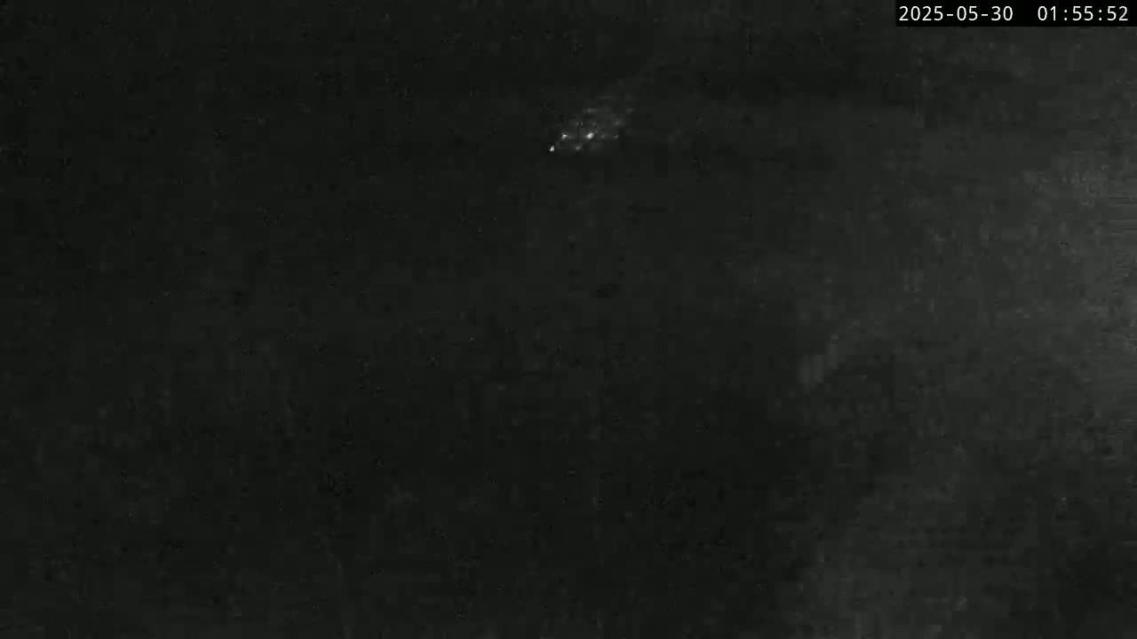A nighttime, dark image shows a small cluster of bright lights in the distance.