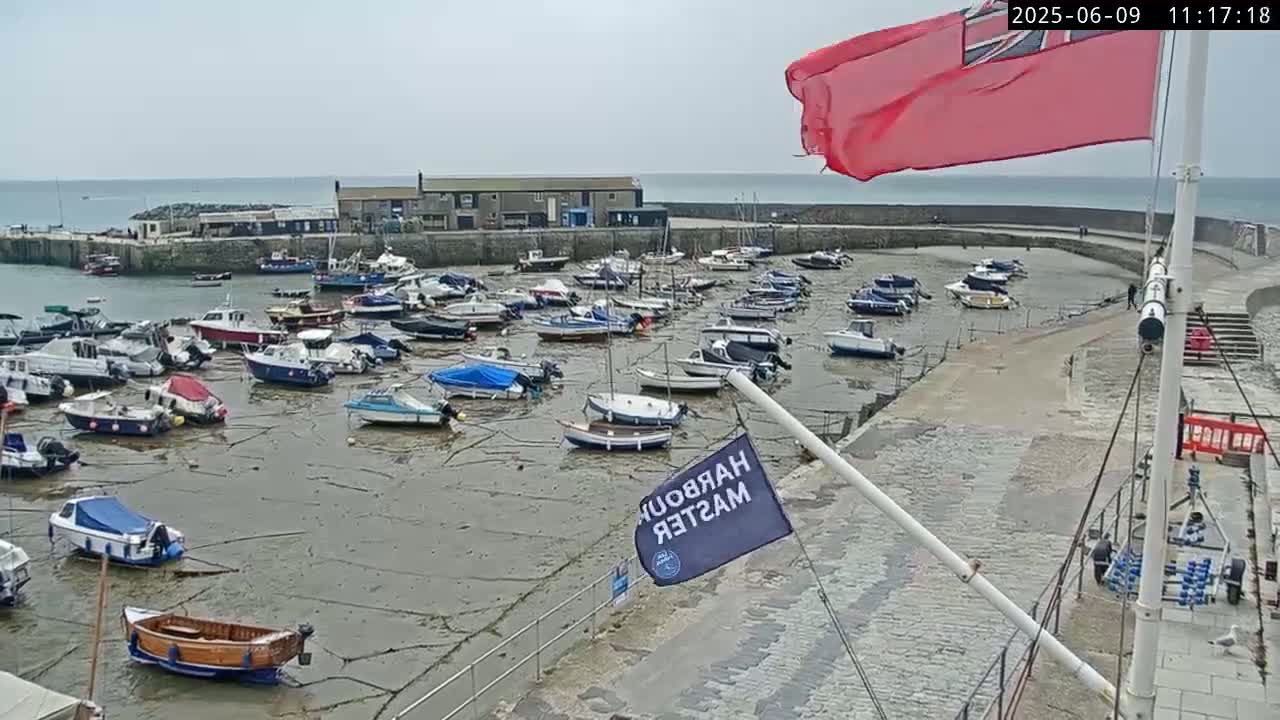 Numerous small boats are resting on the exposed seabed of a harbor on an overcast day.
