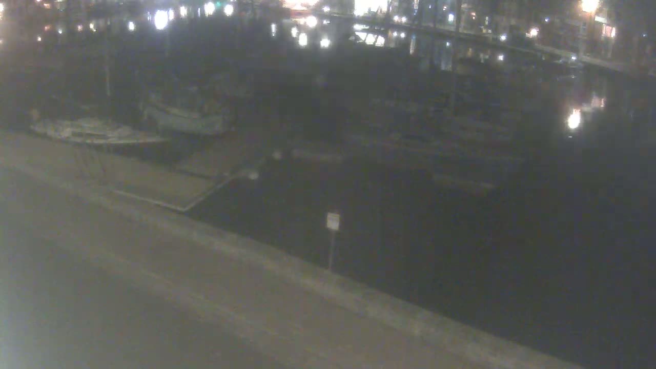 At night, several boats are docked at a waterfront, with dimly lit buildings visible across the water.