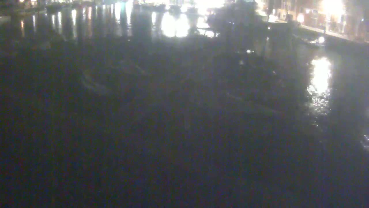Several boats are moored on dark water at night under dim lighting.