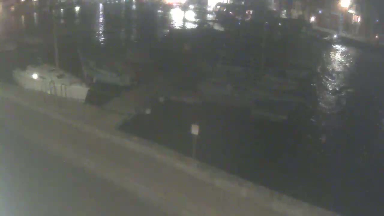 A nighttime view of a marina with several boats docked, showing calm water.