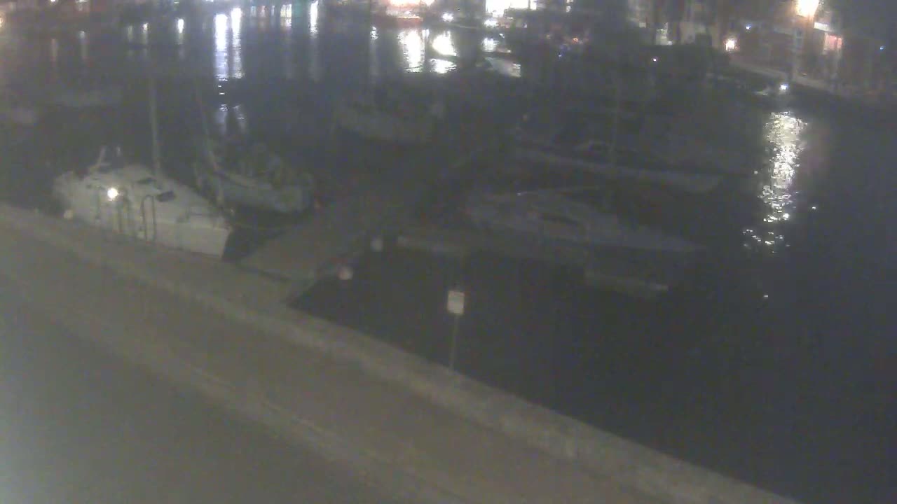 Several boats are moored at a dock at night under a dark, calm sky.