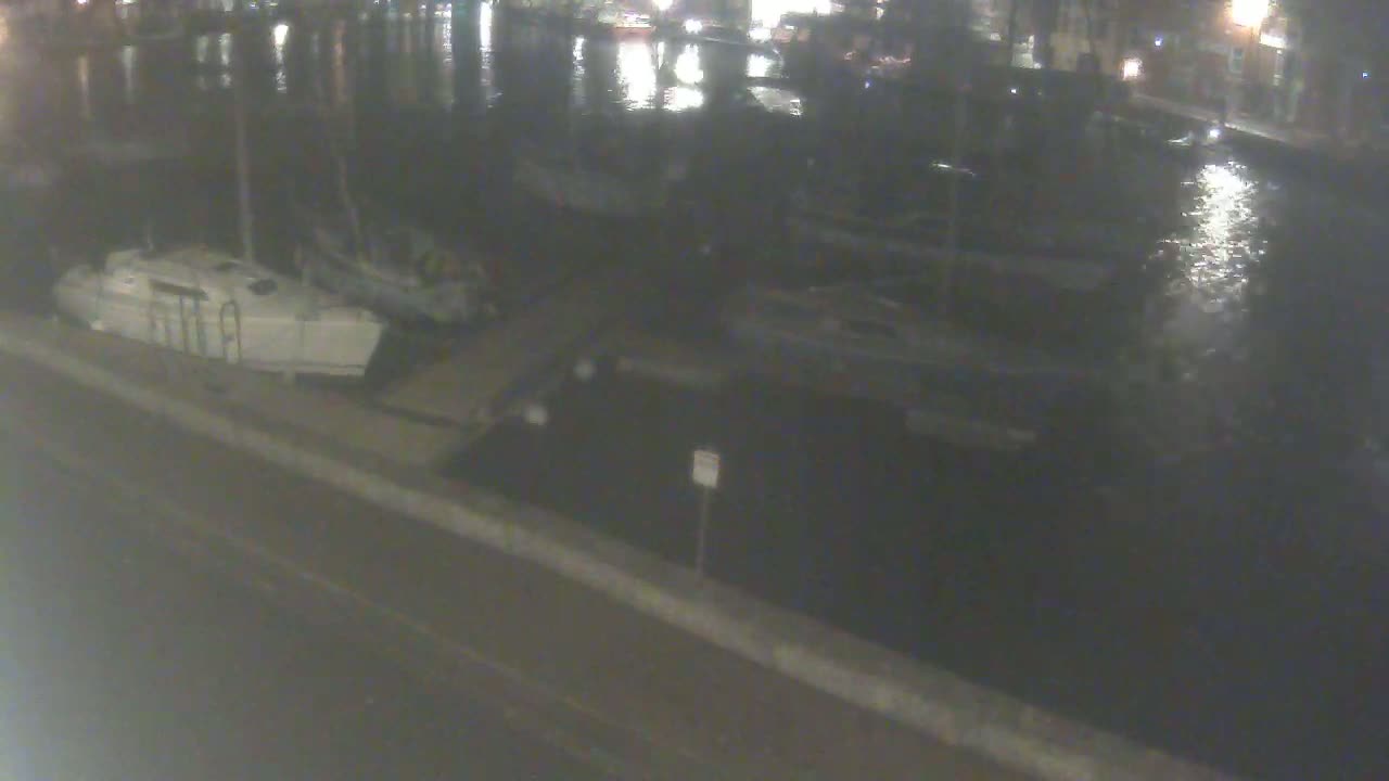 Several boats are moored at a dock at night, on calm water.