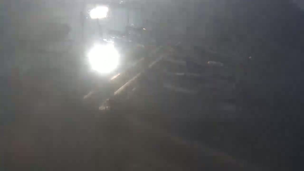 A hazy, bright sun shines on a dark, indistinct outdoor scene that appears to be a roadway or parking lot.