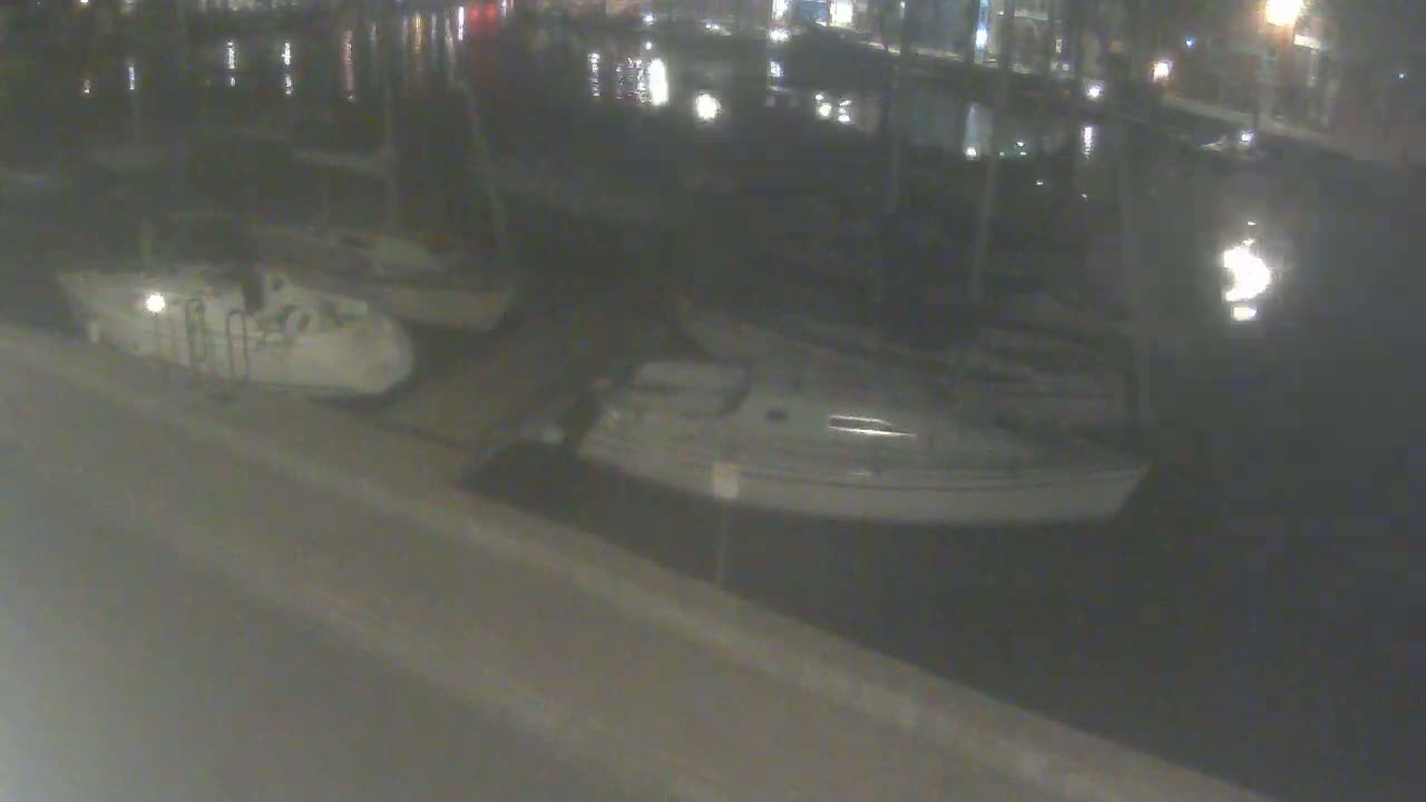 Two small sailboats are docked at a waterfront at night.