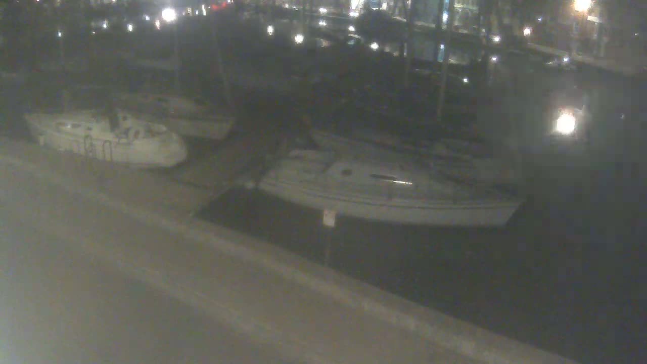 Two sailboats are docked at night next to a paved area.