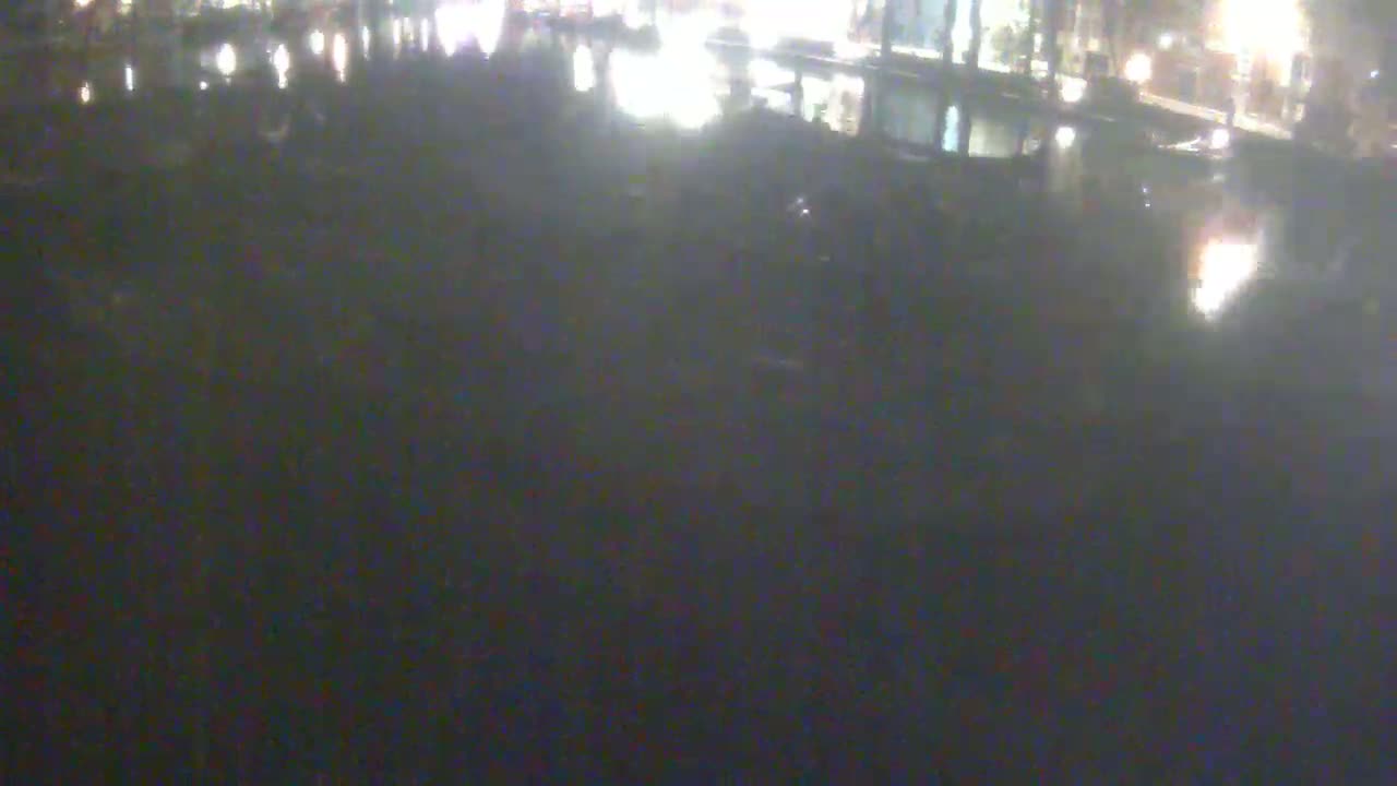 The image shows a dark, nighttime view of a body of water reflecting lights from a distant shoreline.