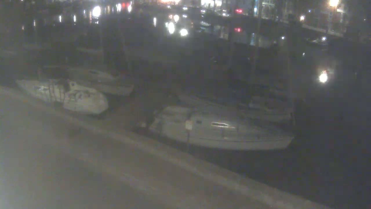 At night, two small white boats are docked next to a dark body of water near a blurry shoreline.