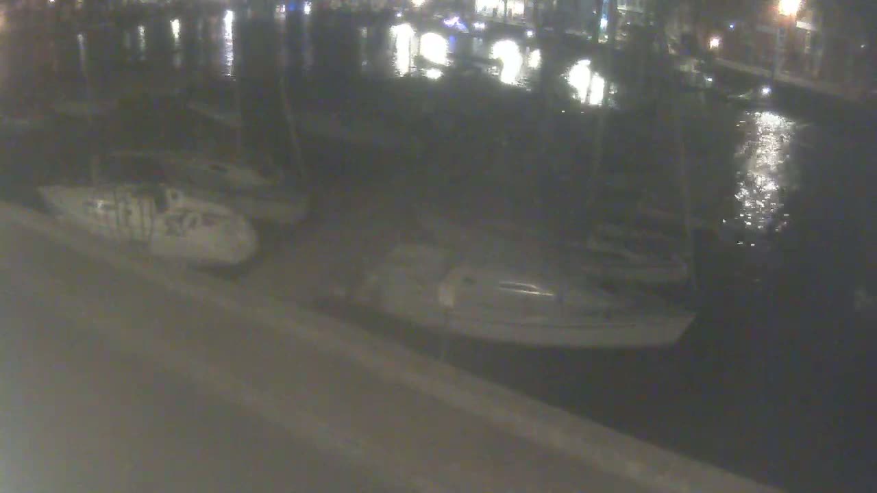 Several boats are moored at a dock at night, with calm, reflective water.