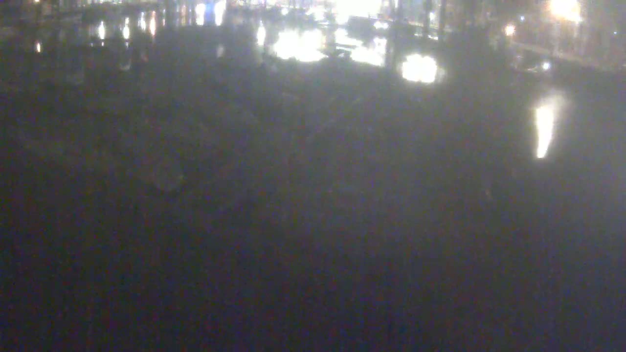 A blurry, dark nighttime outdoor scene shows a wet, reflective surface with indistinct shapes and bright lights in the distance.