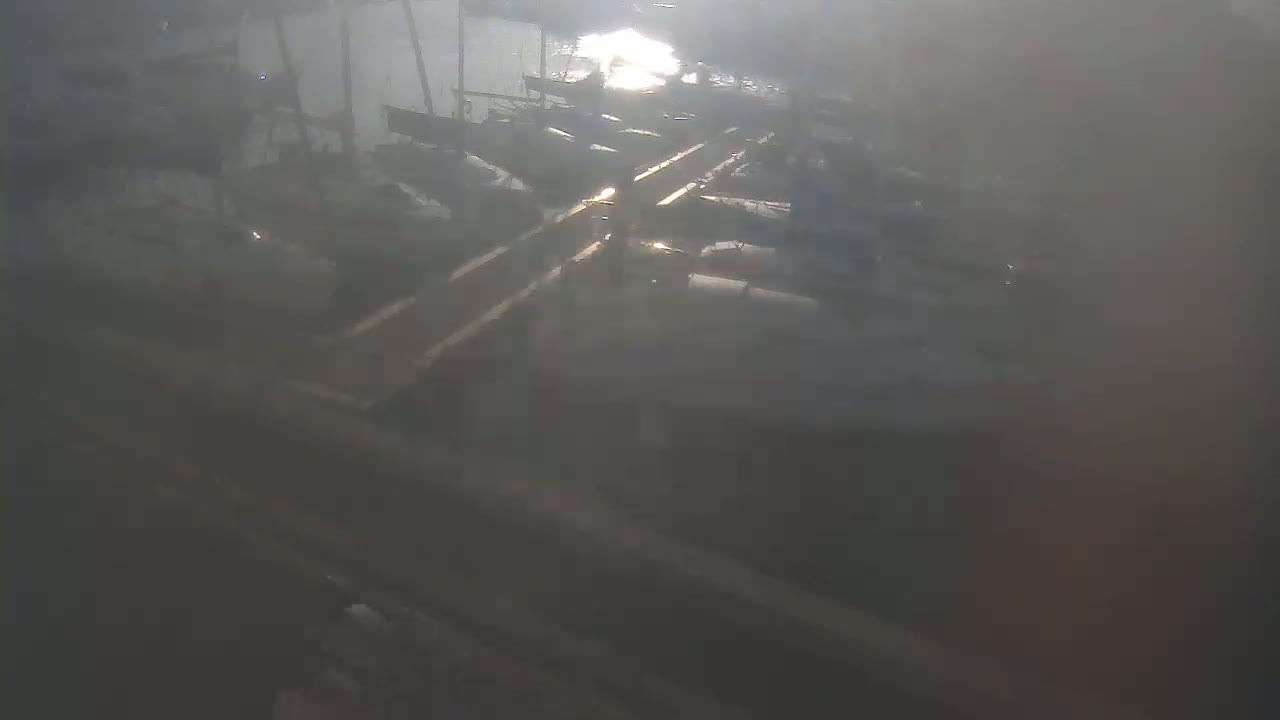 A hazy sun shines on several boats docked at a pier.