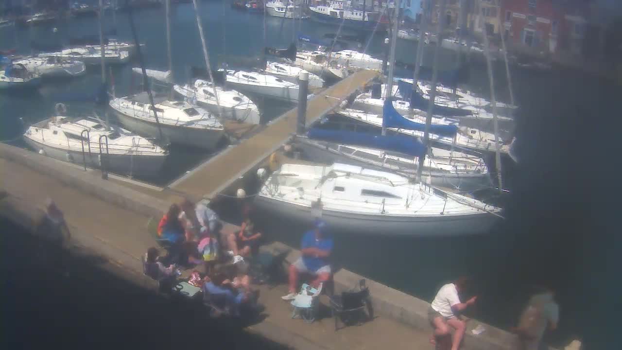 A marina filled with sailboats on a sunny day, where a group of people are sitting on a dock.