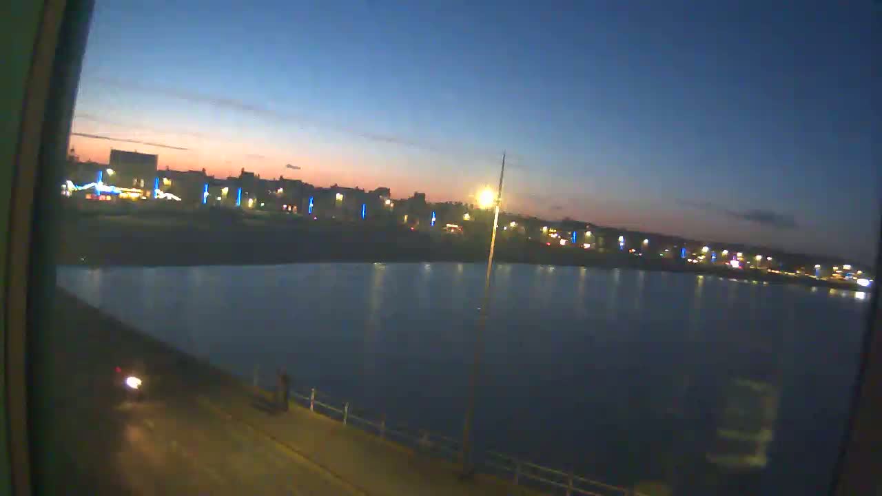 A twilight view shows a calm body of water reflecting the lights of a town at dusk.