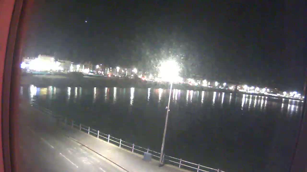 A nighttime view of a calm body of water reflecting the lights of a town across the water.