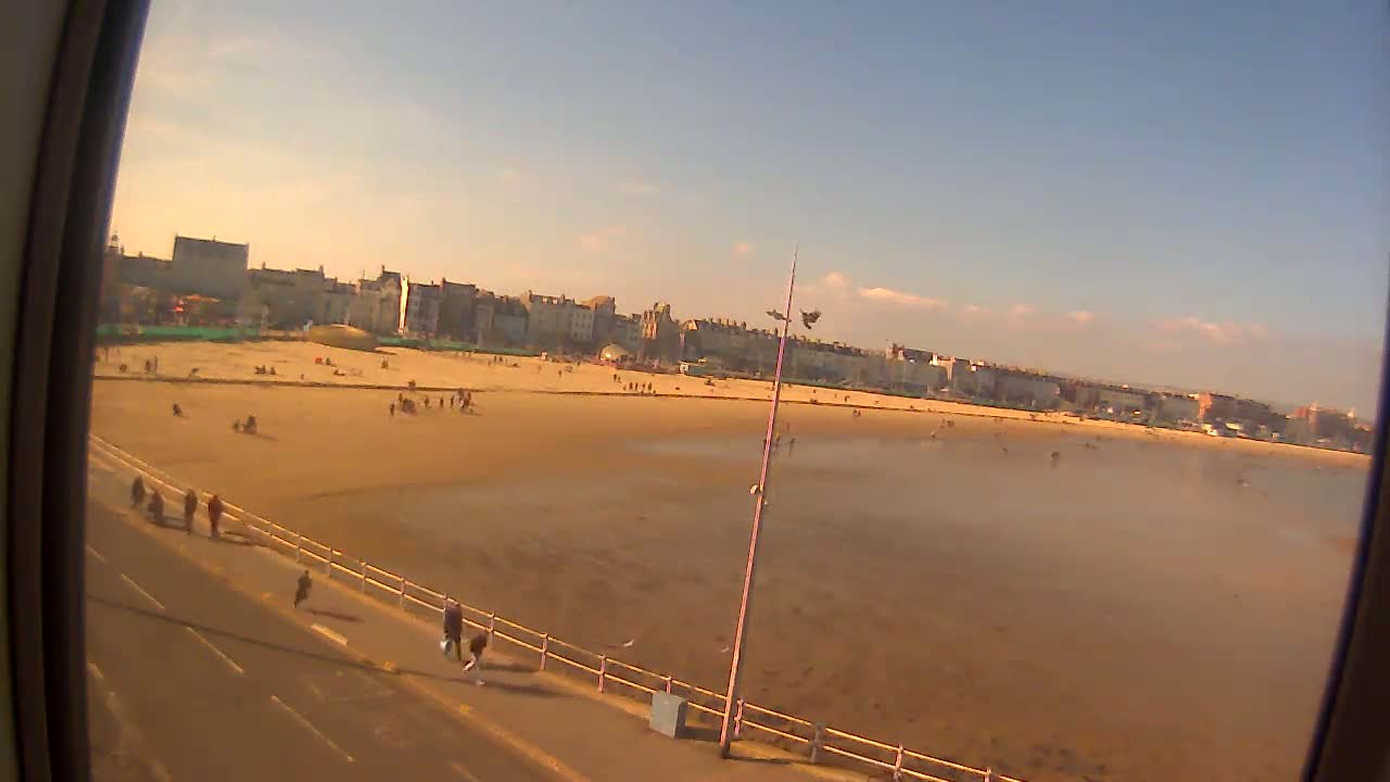 A sandy beach with a few people on it and a town in the background on a partly sunny day.