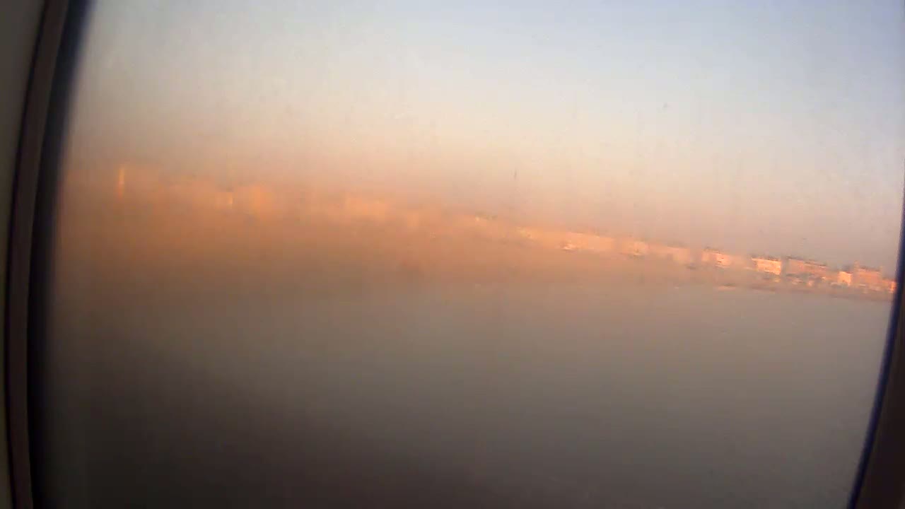 A hazy, dusty view of a distant cityscape is seen through an airplane window during sunrise or sunset.
