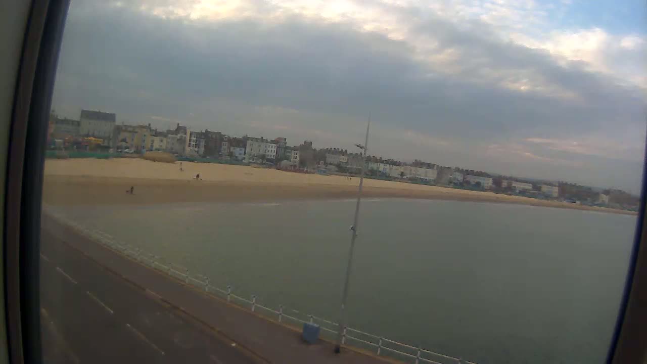 A sandy beach with a few people stretches out before a row of buildings under a cloudy sky.
