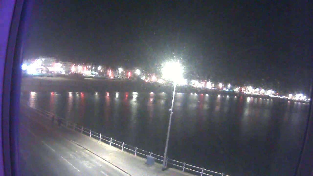 A nighttime view of a calm body of water reflecting the lights of a town across the shore.