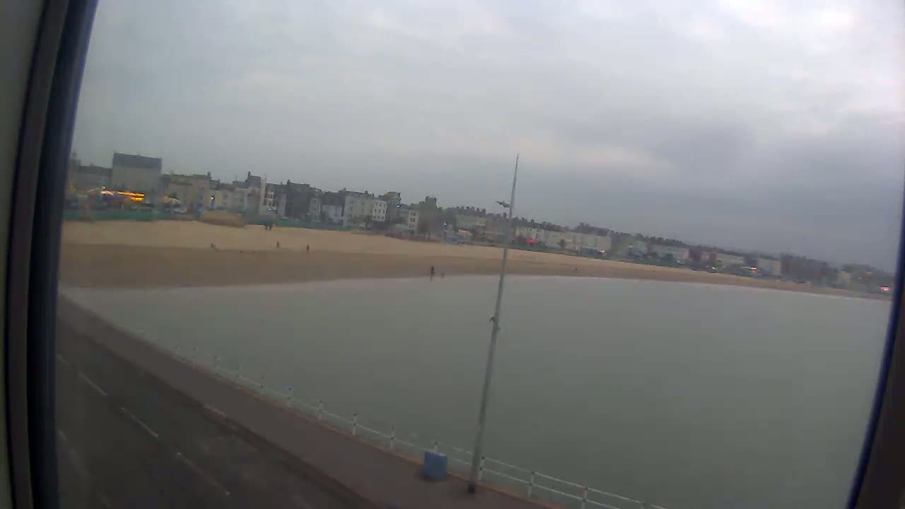 A sandy beach with buildings in the background is viewed from a window, under overcast skies.