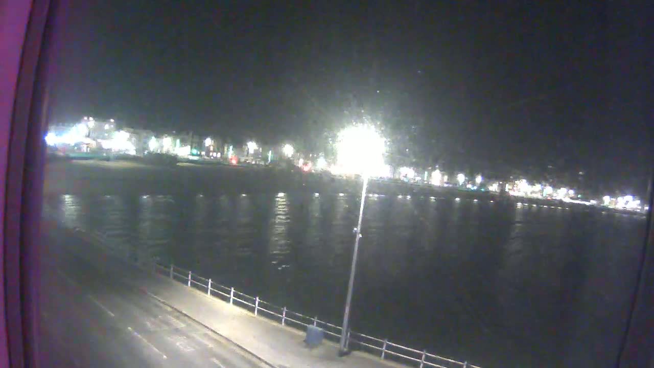 A nighttime view of a calm body of water reflecting the lights of a town across the shore.