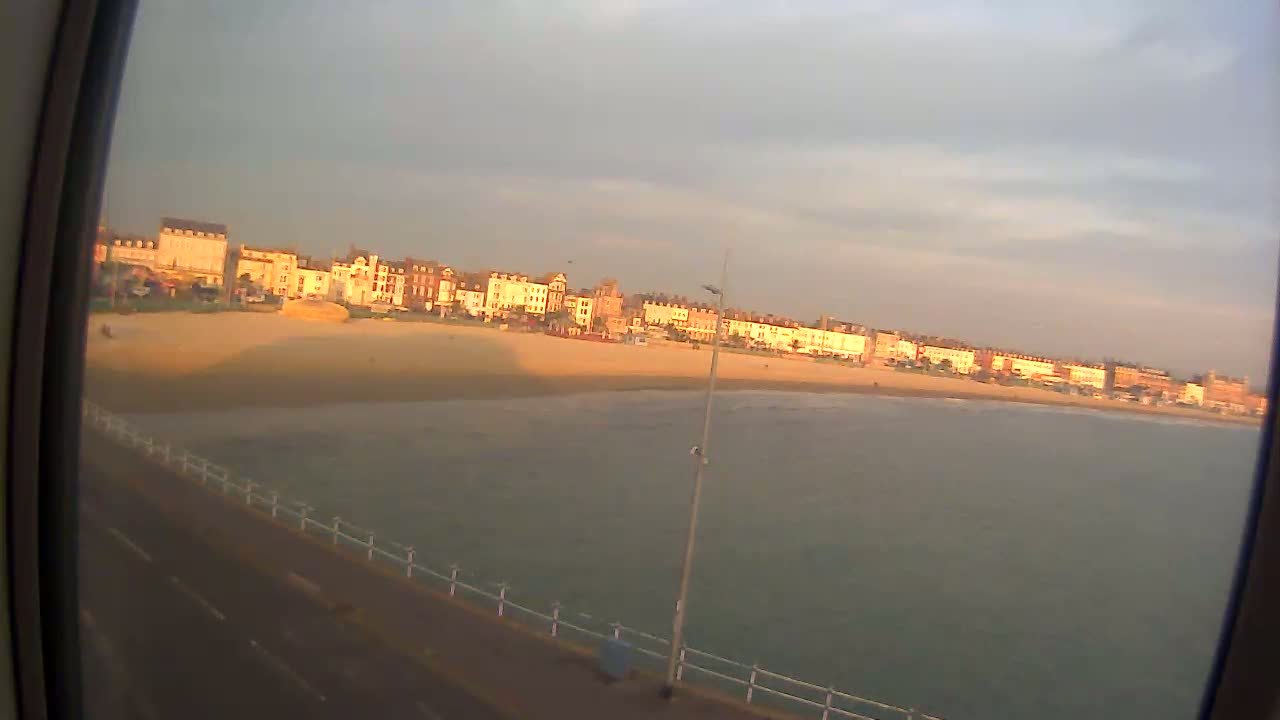 A sandy beach with a row of buildings is visible in the distance under a partly cloudy sky.