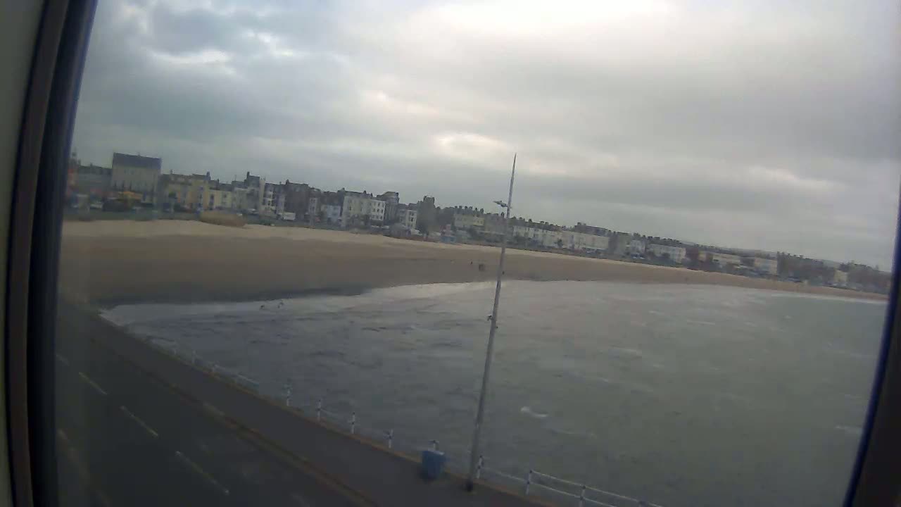 A sandy beach with buildings in the background is viewed from a distance on an overcast day.