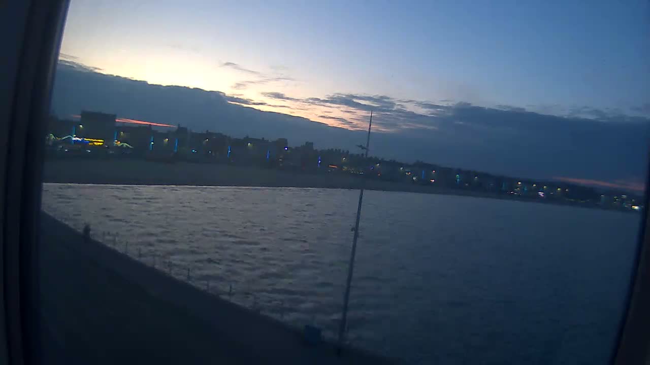 A dark, slightly wavy body of water stretches out before a shoreline of buildings faintly lit at twilight.