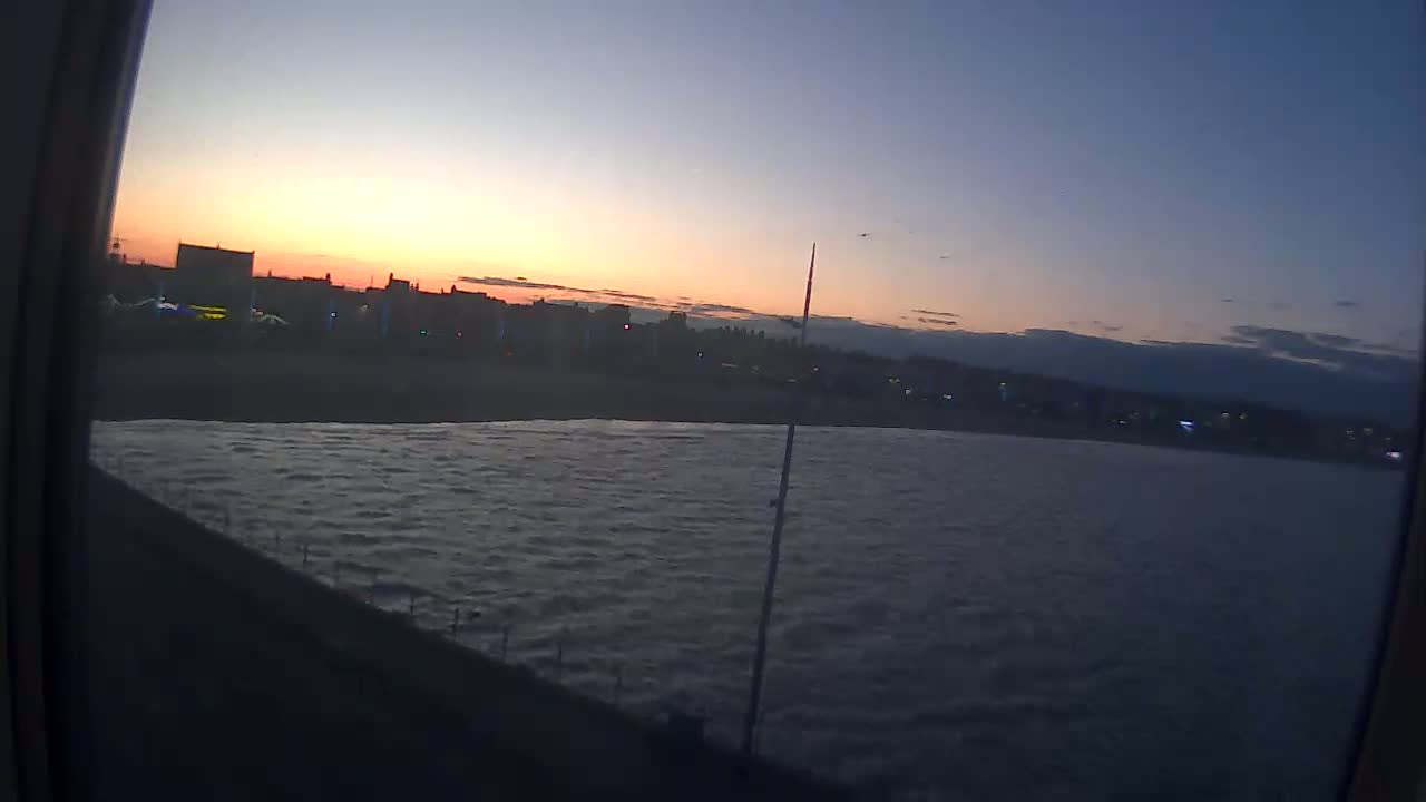A seaside town at sunset is seen from across a body of choppy water.