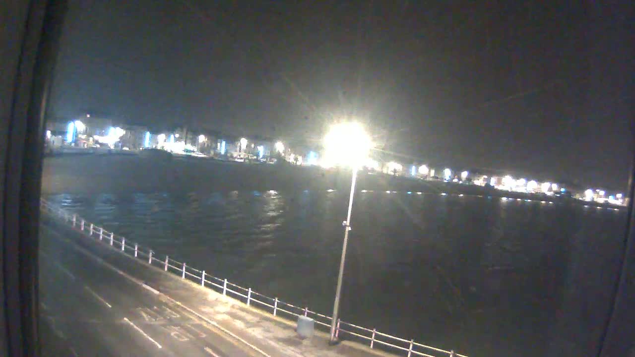 A nighttime view of a choppy body of water next to a waterfront road and a line of buildings with lights on.