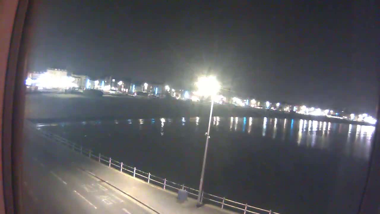 A nighttime view of a calm body of water reflecting the lights of a distant town.