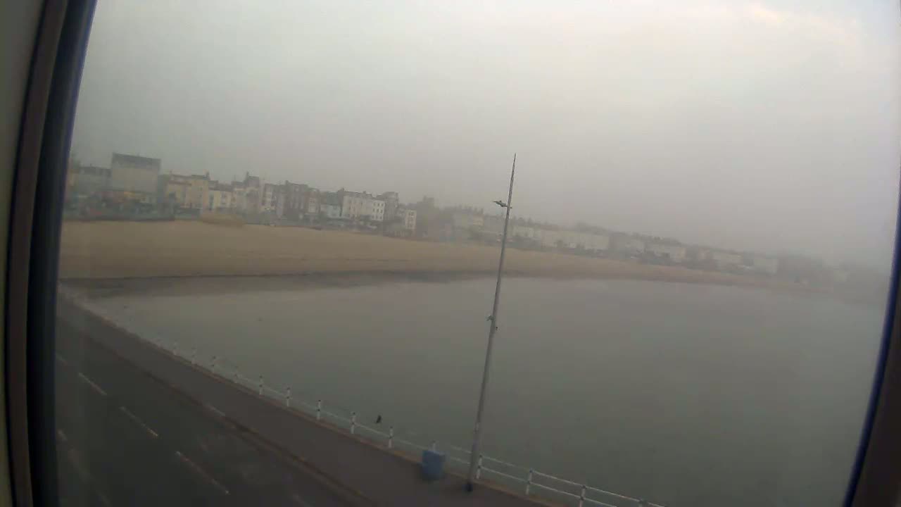 A foggy seaside town is visible from a high vantage point, showing a beach, buildings, and a road along the water's edge.