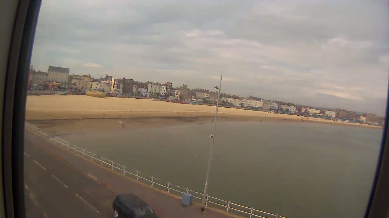 A sandy beach with buildings behind it is seen from a slightly elevated viewpoint on an overcast day.