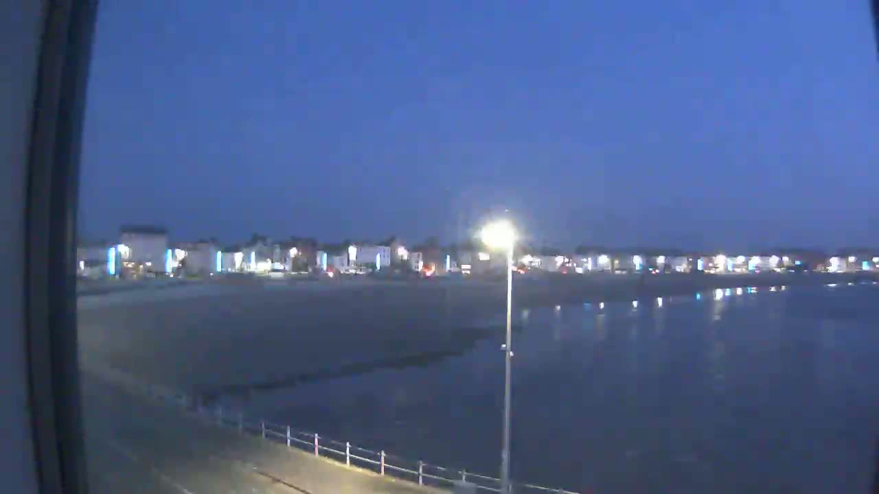 A nighttime view of a beach town with calm water reflecting the lights from buildings along the shore.