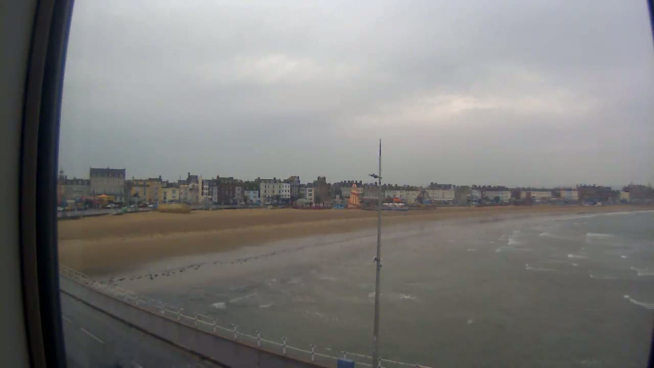 A beach with buildings in the background is seen on an overcast day with choppy water.