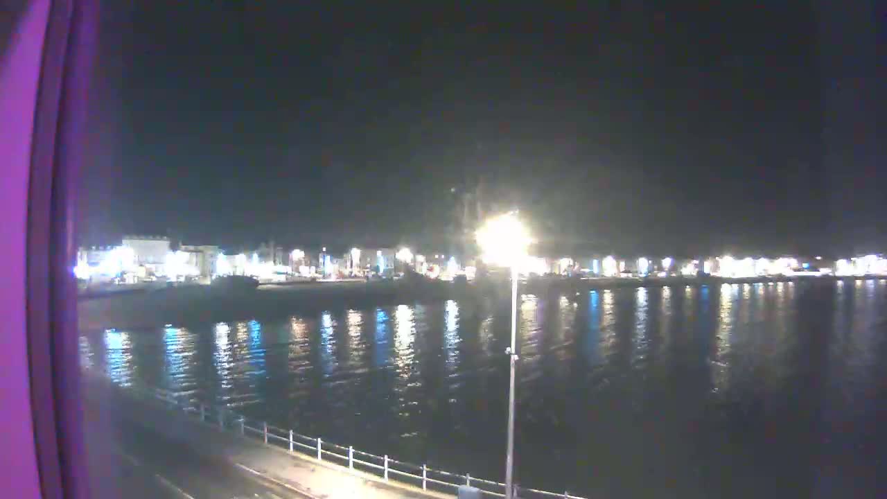 A nighttime view of a calm body of water reflecting the lights of a town across the water.