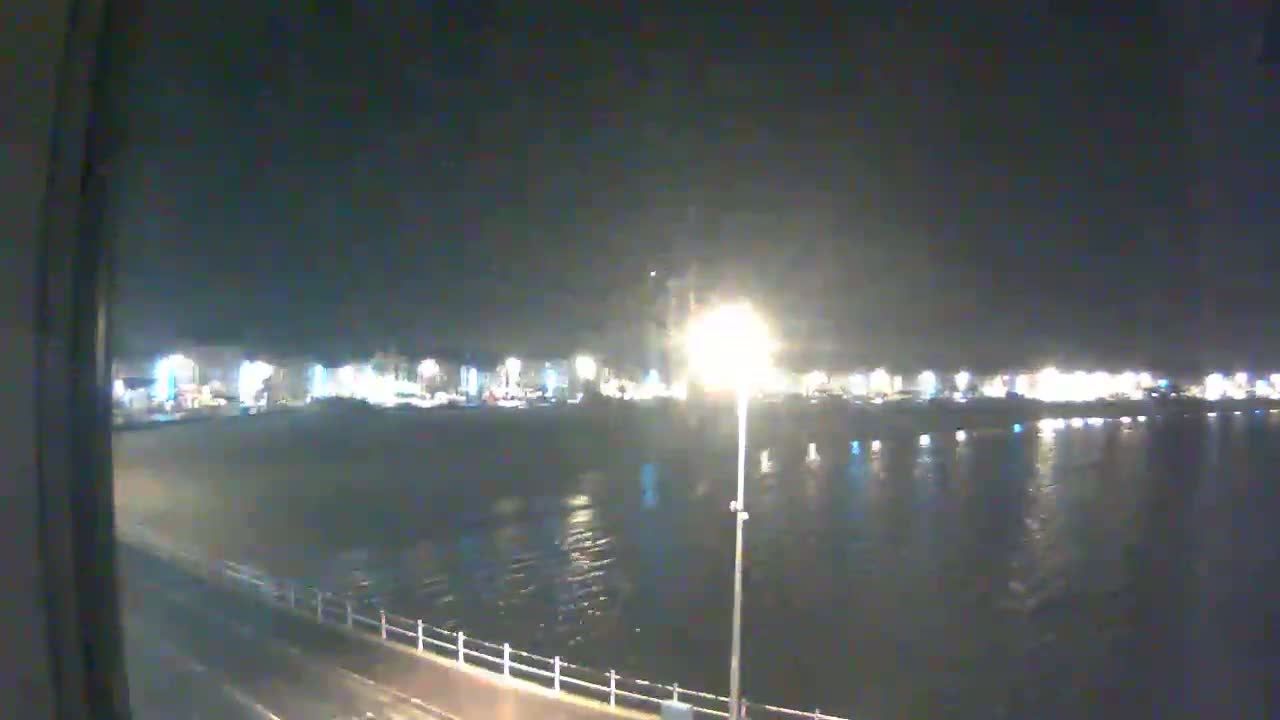 A nighttime view of a calm body of water reflecting the lights of a distant town under a dark sky.