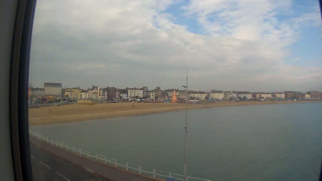 A view from a window shows a sandy beach and calm ocean water, with a row of buildings along the shore under a partly cloudy sky.