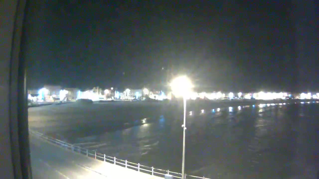 A nighttime view of a dark, calm body of water next to a brightly lit beachfront area.