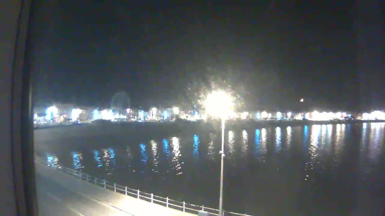 A nighttime view of a calm body of water reflecting the lights of a town across the shore.