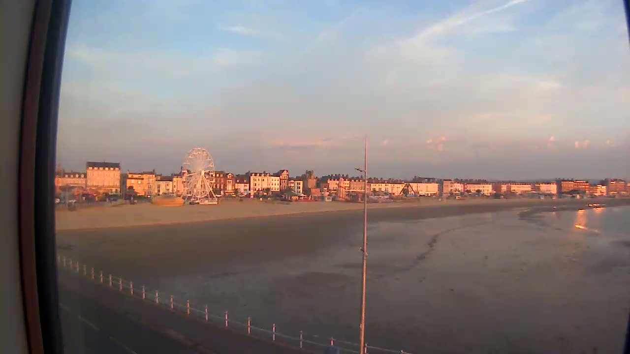A Ferris wheel sits on a sandy beach next to a row of buildings at sunset under a mostly clear sky.