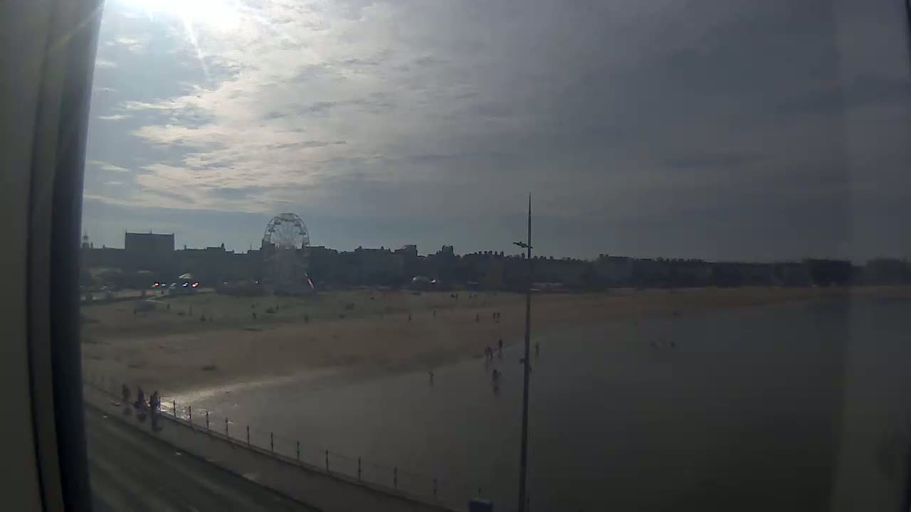 A mostly sunny day shows a beach with a Ferris wheel in the background.